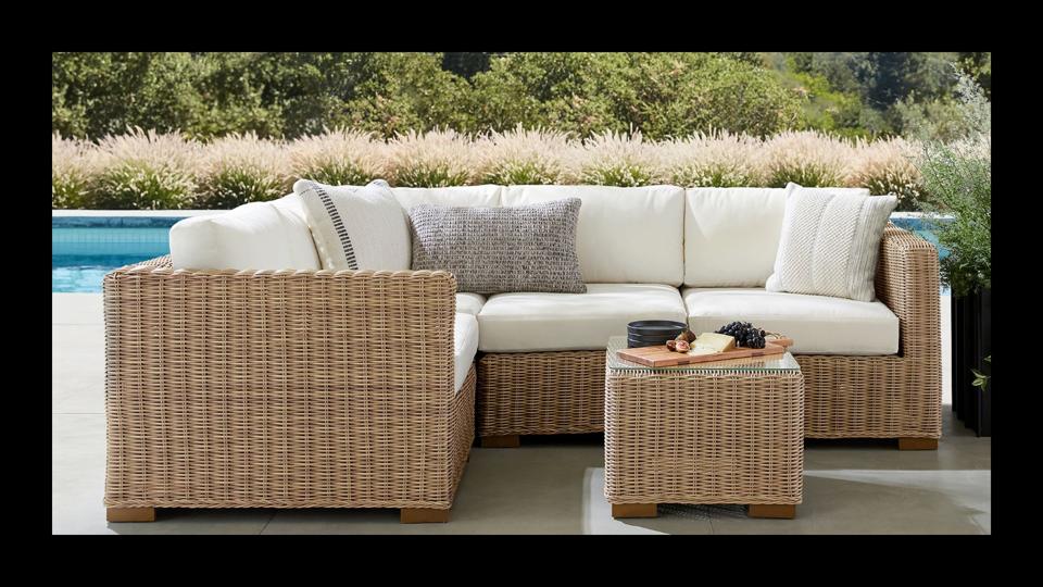 The Pottery Barn Huntington Wicker Sectional featured in a lush backyard with a pool in the backdrop. 