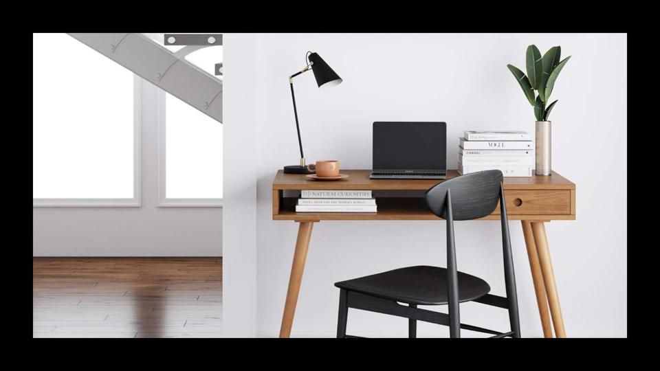 A wooden desk topped with a laptop, lamp, tea cup, books and plant and a black chair featured in a modern home. 