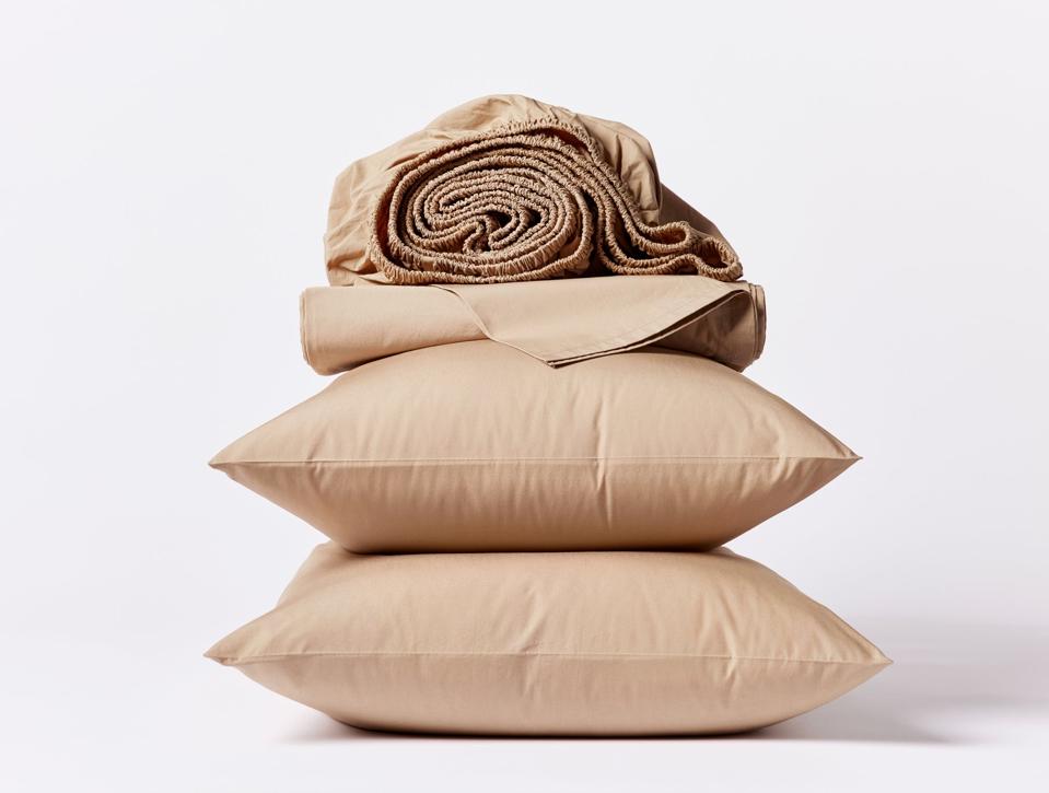 Coyuchi Organic Percale Sheet Set stacked on top of two pillows on a pale background.