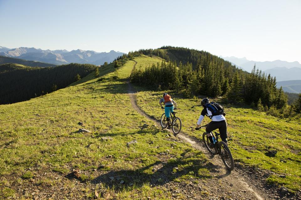 Two young men ride mountain bikes down a trail in the Rocky Mountains of Canada