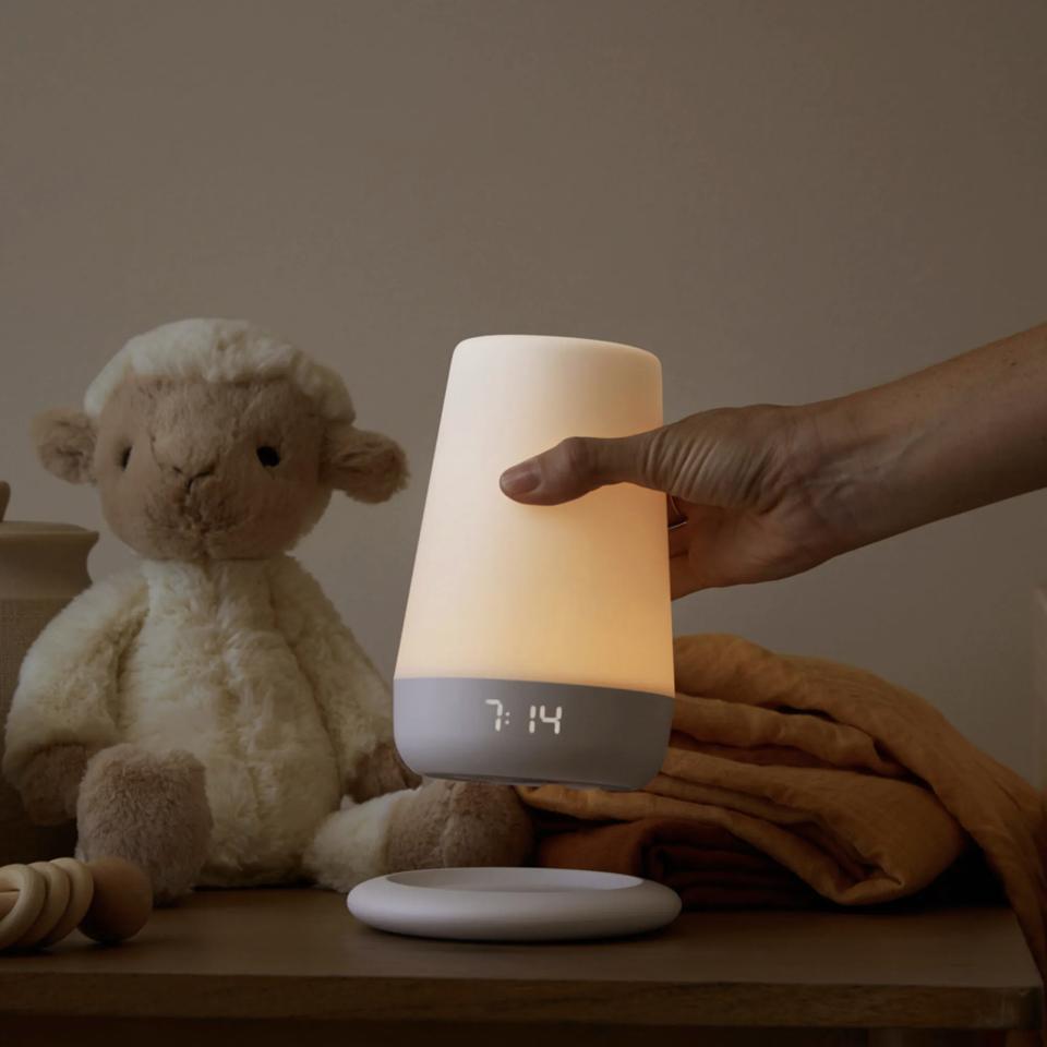 A hand putting the Hatch Rest+ down on a table in front of a stuffed animal and blanket. 