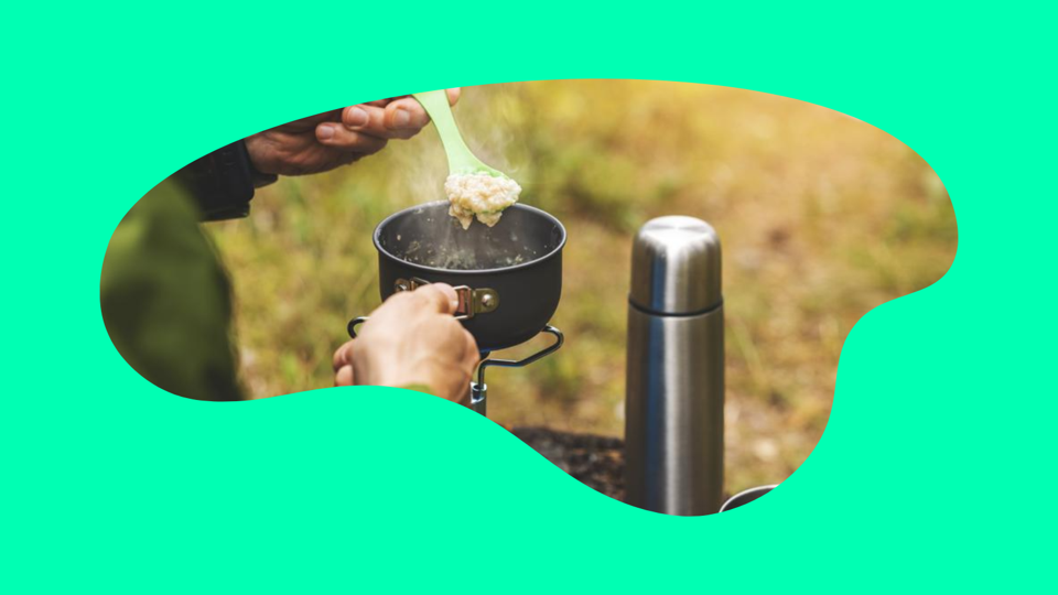 A man prepares a pot of food over a stove next to a thermos while backpacking 