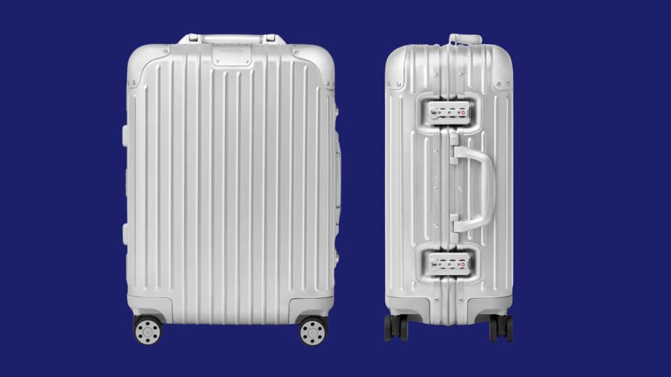 A Rimowa aluminum suitcase against a dark blue background.