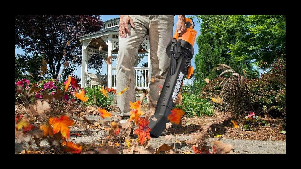 A leaf vacuum in action blowing leaves in a front yard with a gazebo in the background. 