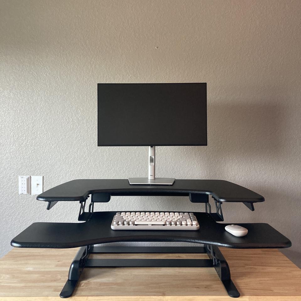 A black VariDesk Pro Plus 36 on a bamboo desk in front of a grey wall