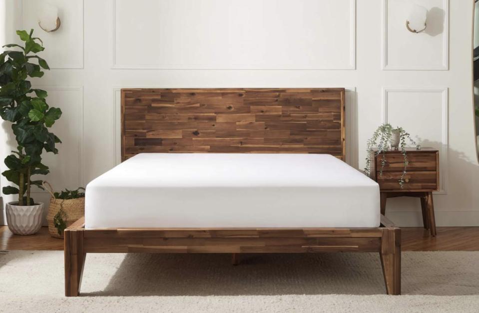 The Silk & Snow Wooden bed frame with a mattress on top and a nightstand beside it. 