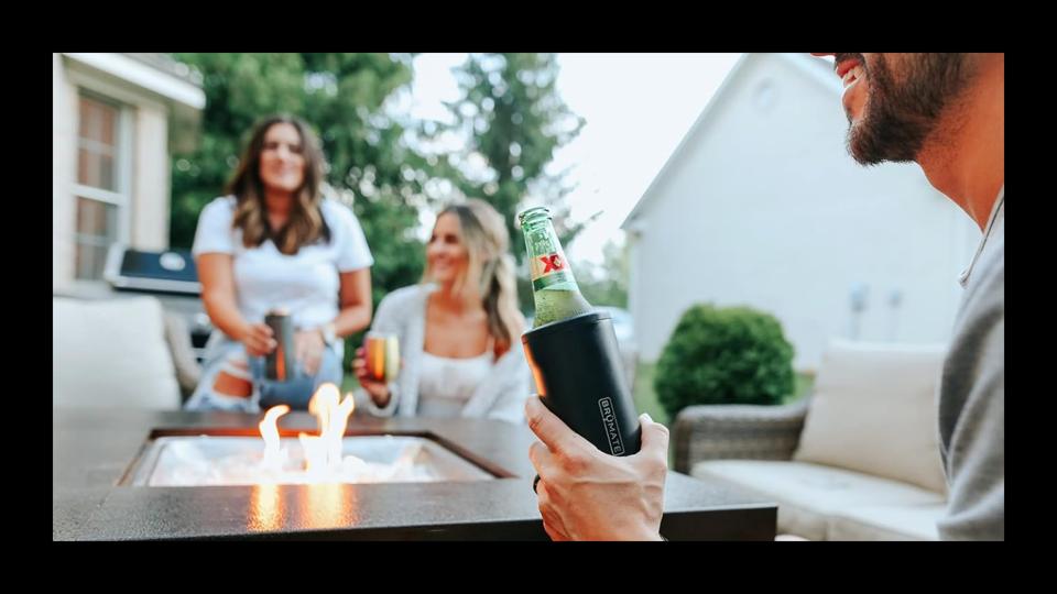 A man holding a bottle covered in a Brumate koozie while two women look on in the background.