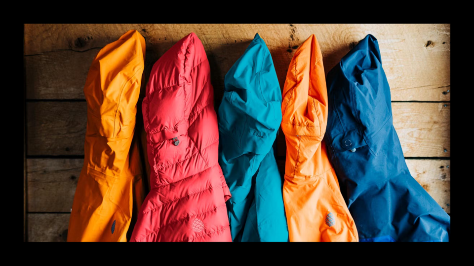 Four jackets on a coat rack over a wooden wall