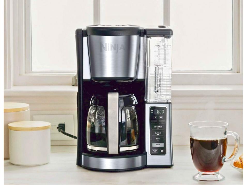 black ninja 12-Cup drip coffee maker and clear cup of coffee on white counter next to window