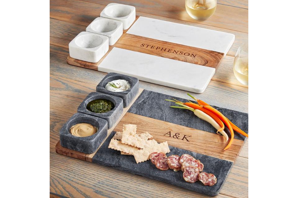 2 personalized charcuterie/cheese boards in marble white and slate gray with wooden accents on wooden table with 2 stemless glasses of white wine