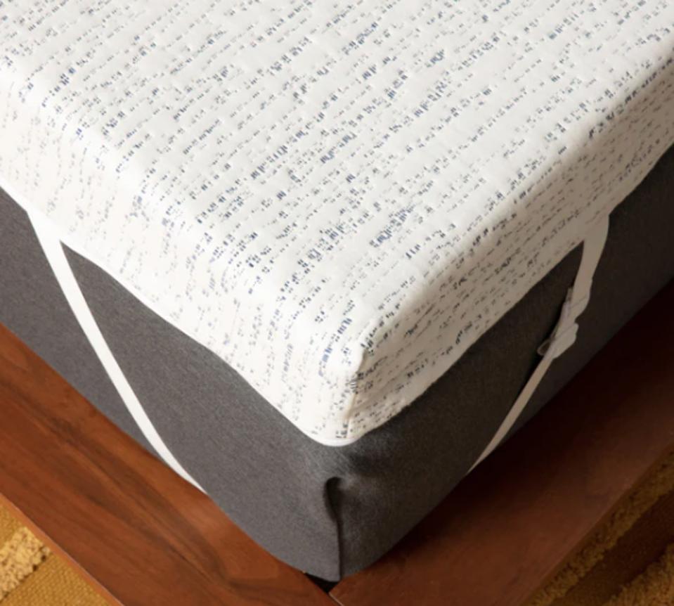 A white mattress topper on top of a mattress above a wooden floor. 