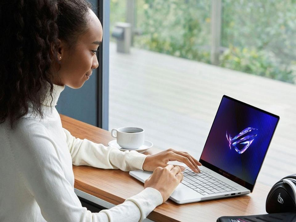 A young black woman using the ASUS ROG Zephyrus G14 in the window seat of a cafe