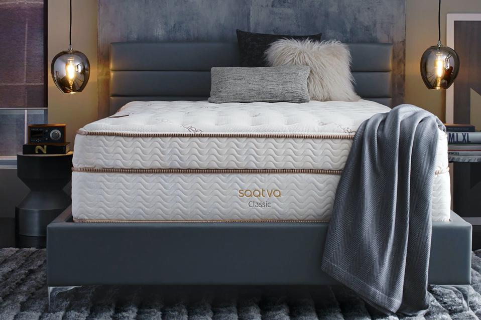 The Saatva Classic on a gray bed frame with a blanket draped over the foot. 