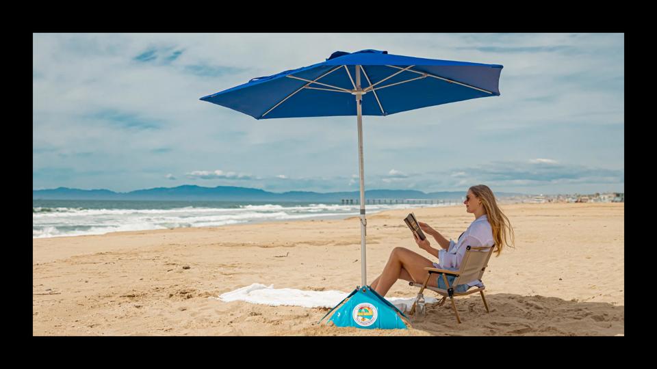 A woman at the beach reading and sitting under a blue umbrella from Beac