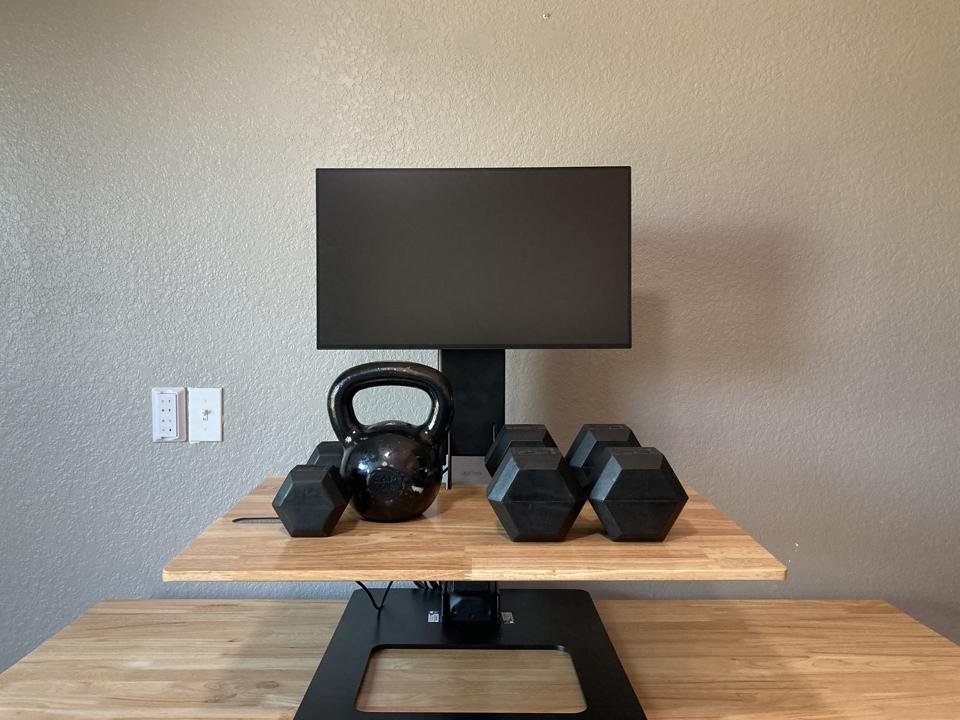 The Uplift E7 Standing Desk with multiple weights on it as well as a monitor in front of a grey wall 