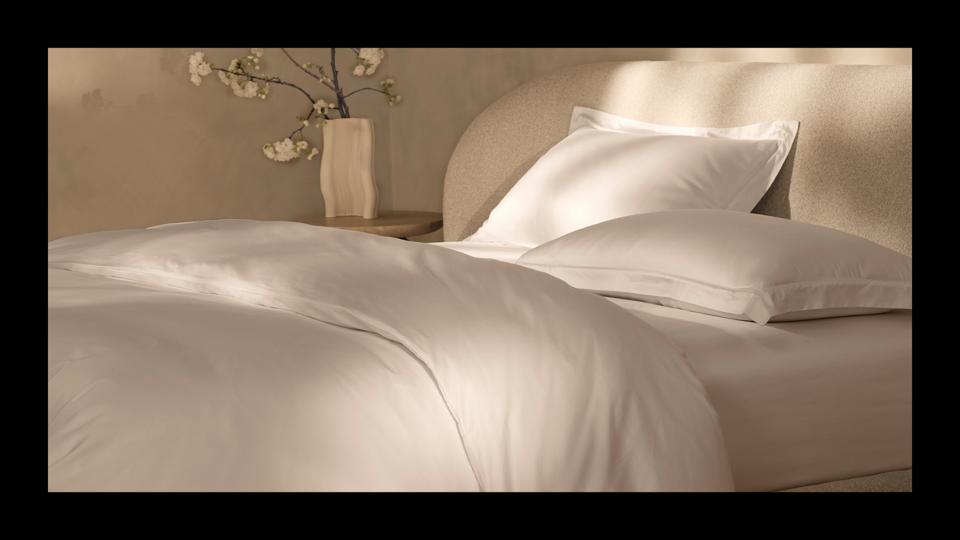 Boll & Branch's Summit Supima sheet set in white on a cream bed frame with a flower vase