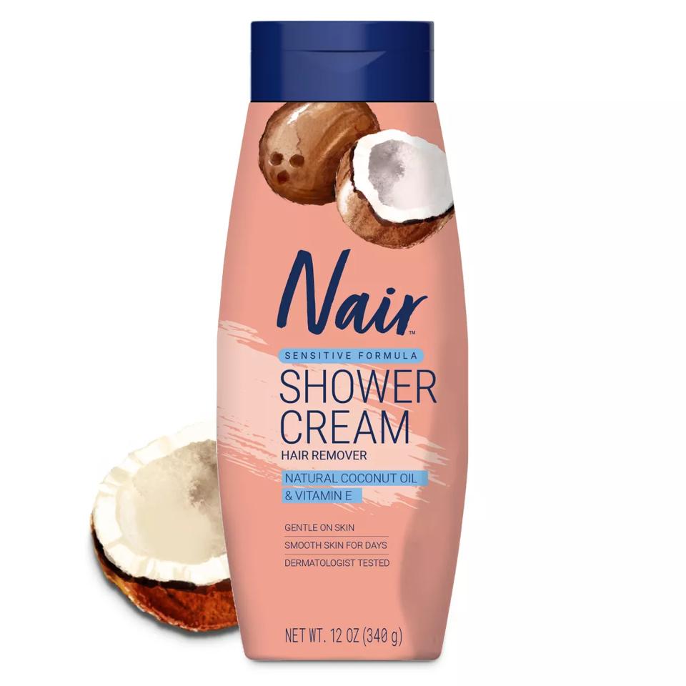 Nair Sensitive Shower Cream Hair Remover with coconut behind bottle on white background.