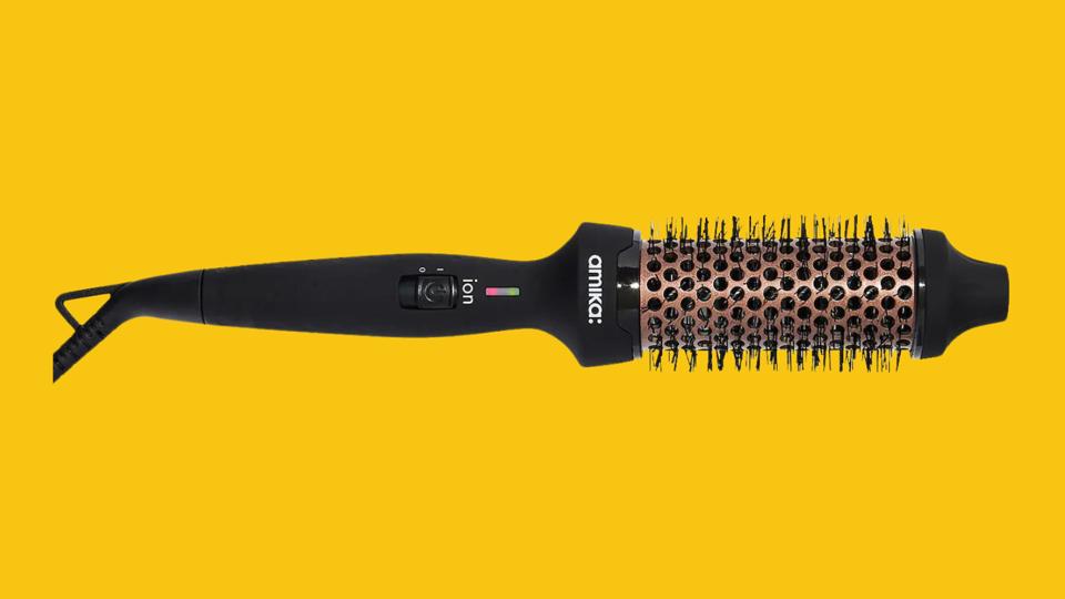 The black Amika Blowout Babe Thermal Brush on a mustard yellow background