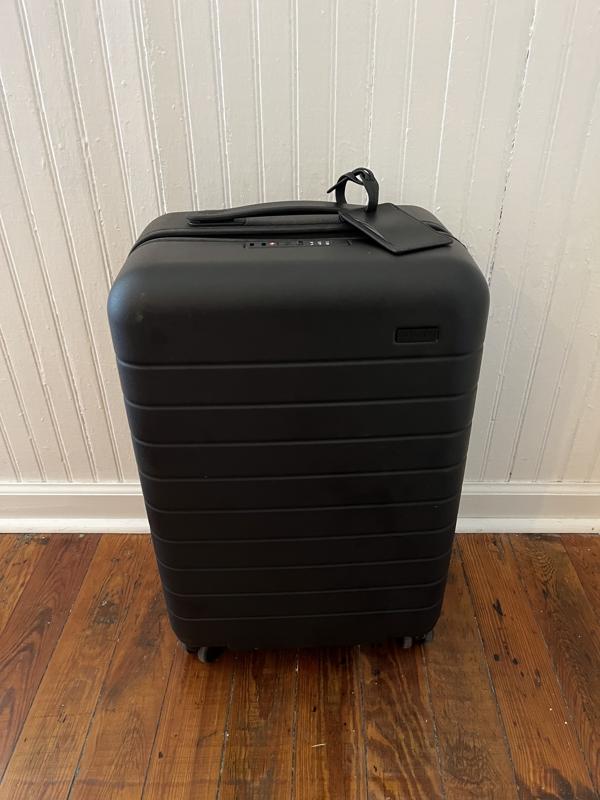 Black Away The Carry-On suitcase against a white wall.