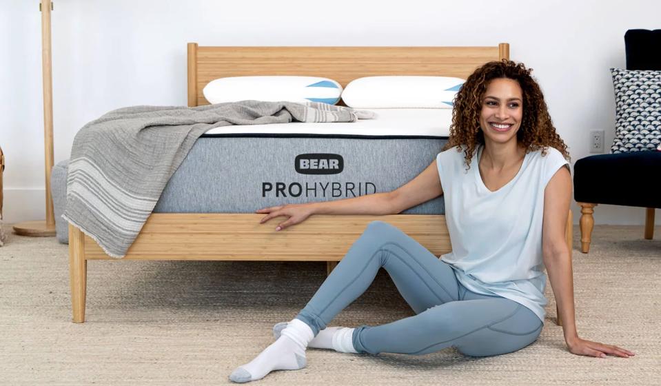 A woman lying on the ground next to the Bear Pro Hybrid mattress.