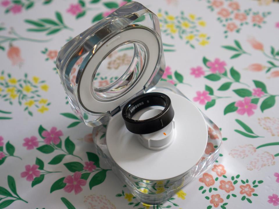 The Samsung Galaxy Ring and charger on a floral background