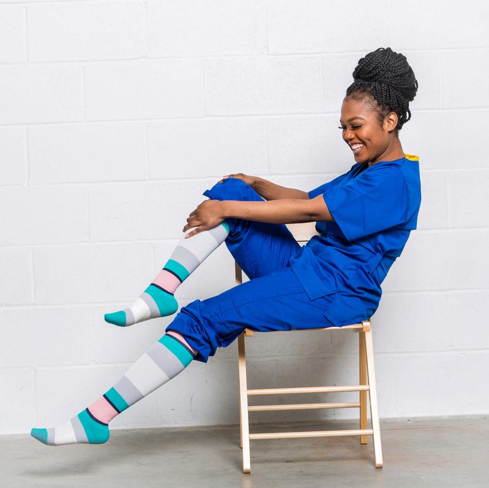 A woman in blue scrubs wearing the Trtl Travel Flight Compression Socks 