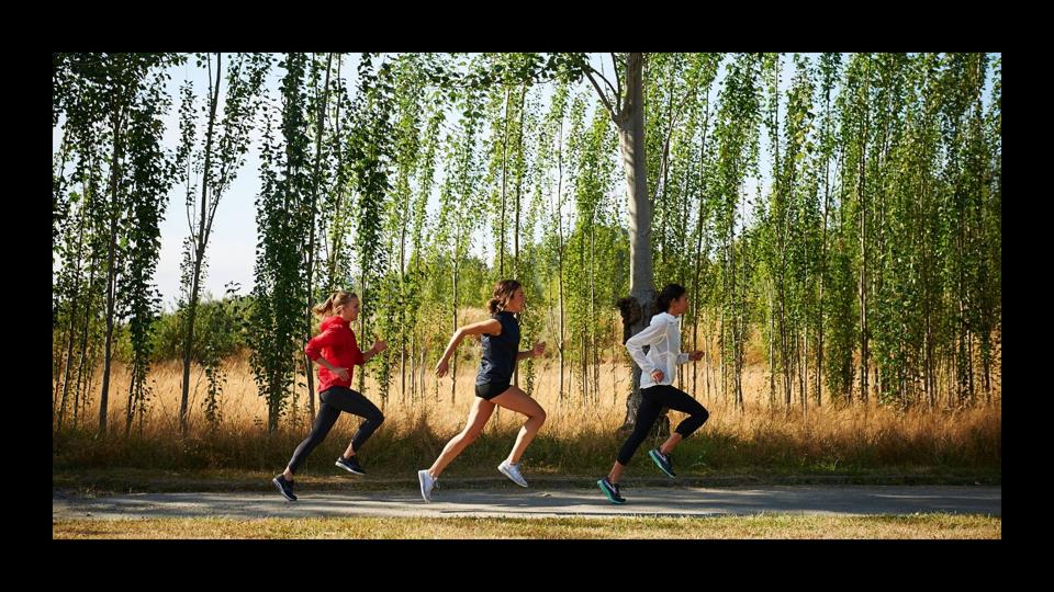 Three women running on a sunny road next to trees