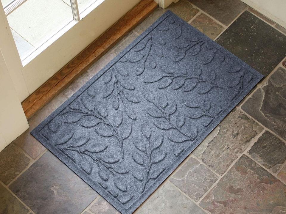 A blue Bungalow Flooring Waterhog Door Mat on a stone floor in front of a door