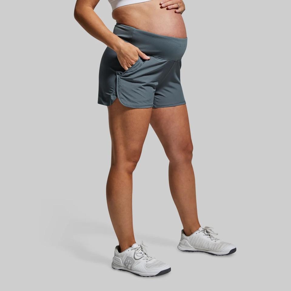 A dark-skinned woman wearing the Born Primitive Maternity Short on a grey background