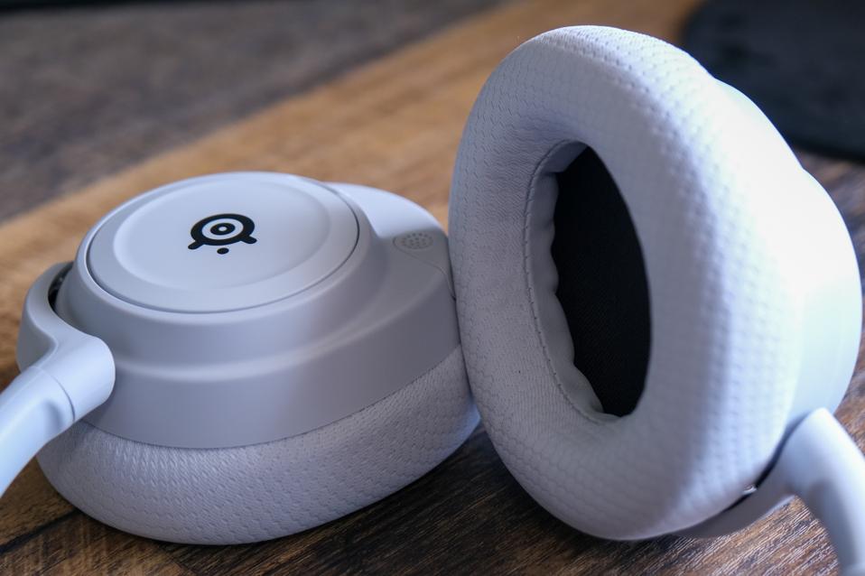 Ear pads of a white SteelSeries Arctis Nova 7 Wireless on a wooden table.