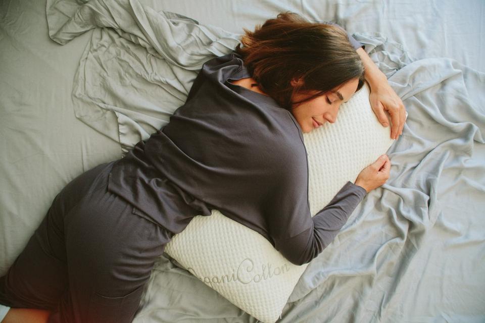 Woman hugging Nest Bedding Easy Breather Natural Latex Pillow on a bed.