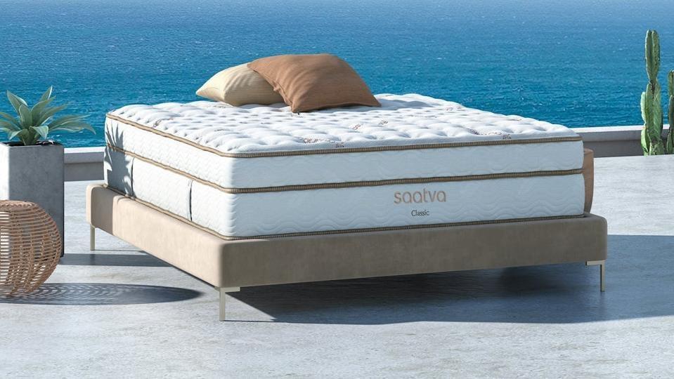 The Saatva Classic Mattress on top of a brown bed frame next to the water. 