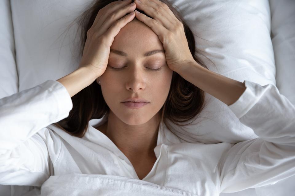 Best Migraine Relief Products: Top view depressed woman suffering from headache, lying in bed