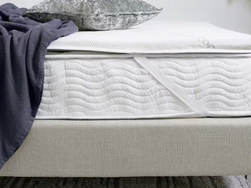 The Saatva High-Density Foam Mattress Topper shown on a mattress with a pillow and blanket.