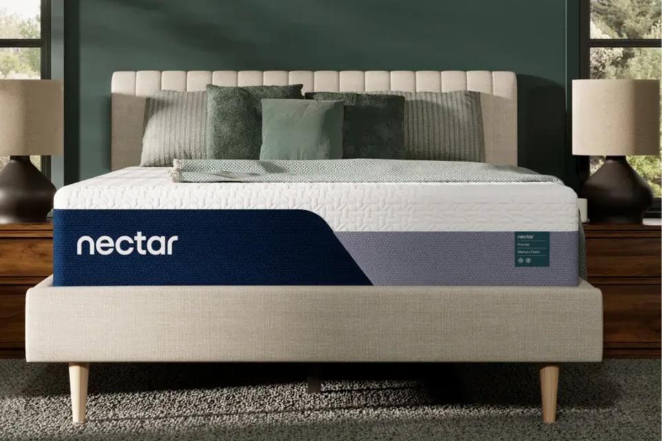 The Nectar Premier Memory Foam Mattress on a bed frame with green pillows and a blanket on top.