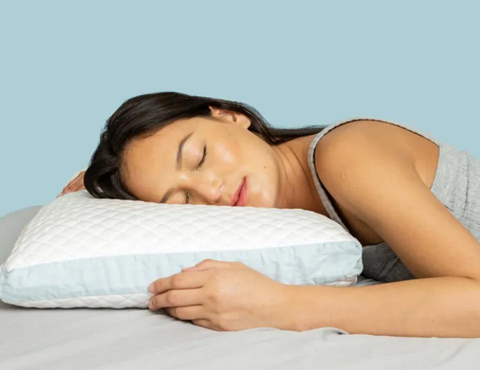 A woman lying on a Pluto Pillow with her eyes closed facing the camera