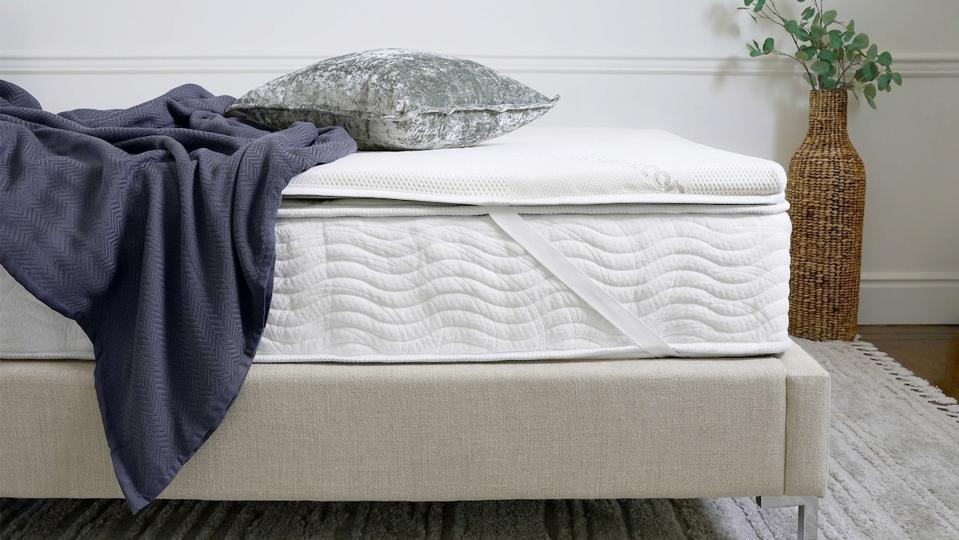 The High-Density Foam Mattress Topper from Saatva on top of a white mattress and tan bed frame. 