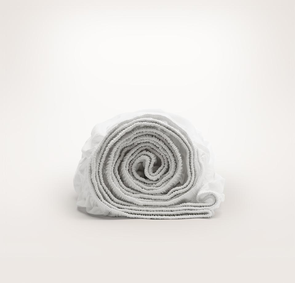 Boll & Branch fitted sheet rolled and seen from the side on a gray background.