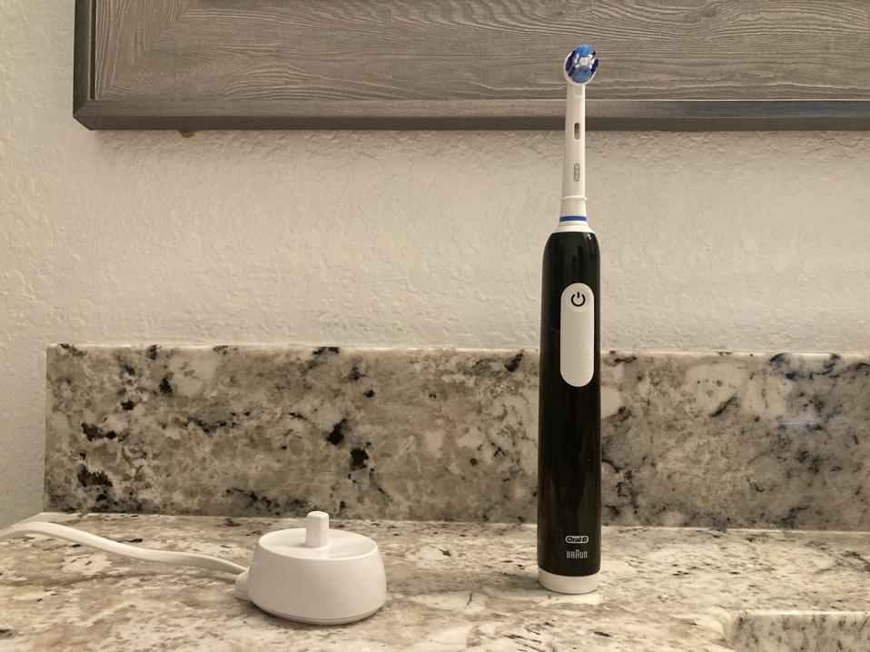 The Oral-B Pro 1000 electric toothbrush along with the white charging base on a countertop