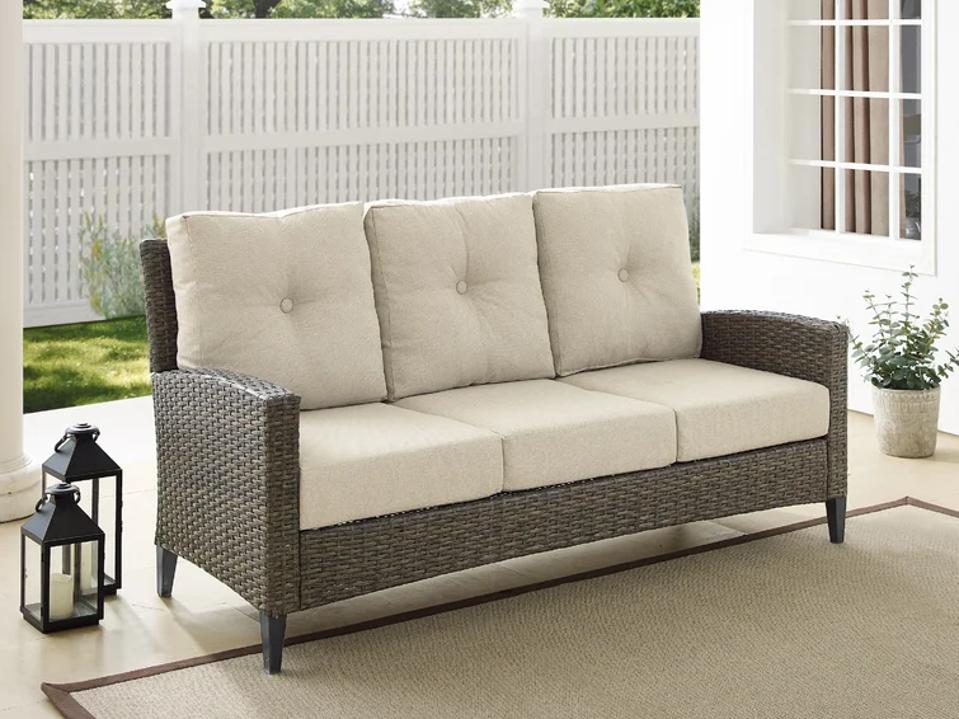 brown Crosley Rockport Wicker Outdoor Patio Sofa with white linen cushions outside. 