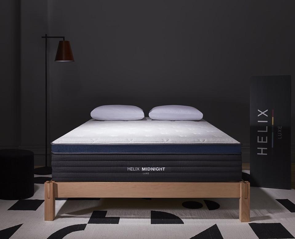 Helix Midnight Luxe set up on a light wood bed frame in a dark room with patterned floor