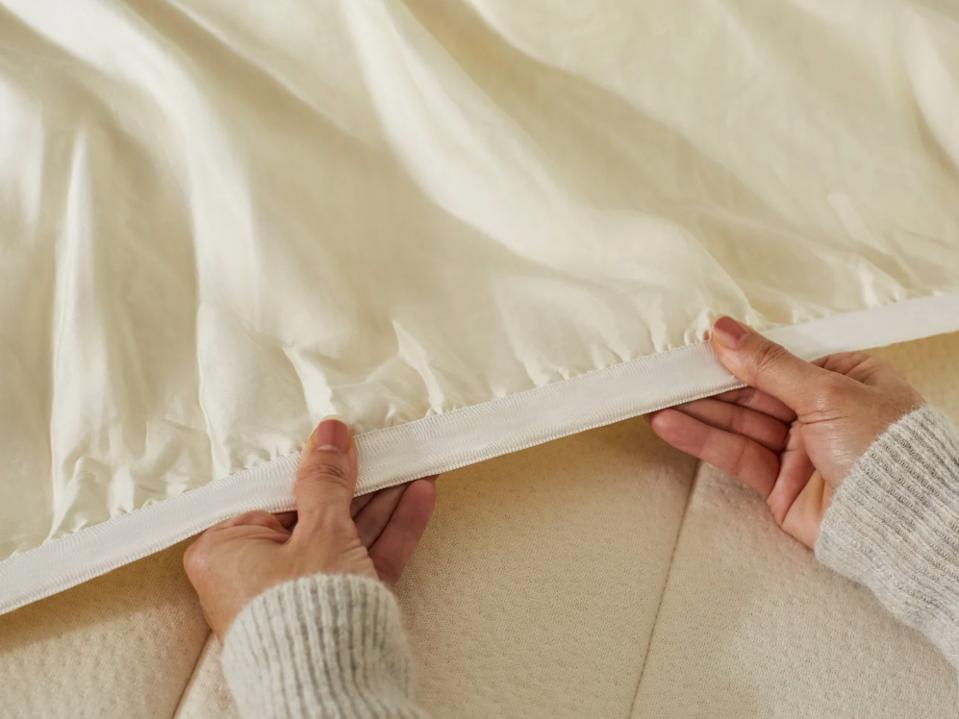 A person's hands stretching the Birch Organic Mattress Pad over mattress.