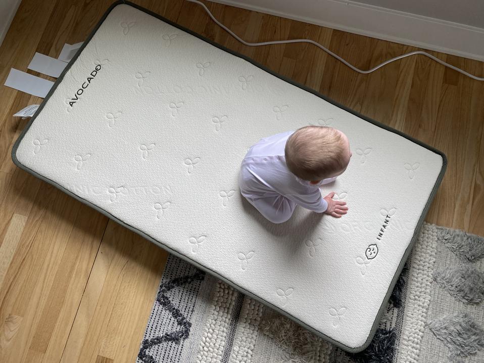 A baby sitting on a bare Avocado Crib Mattress on the floor.