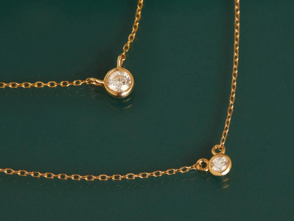 Two Aurate XL Diamond Bezel Necklaces on a green background.