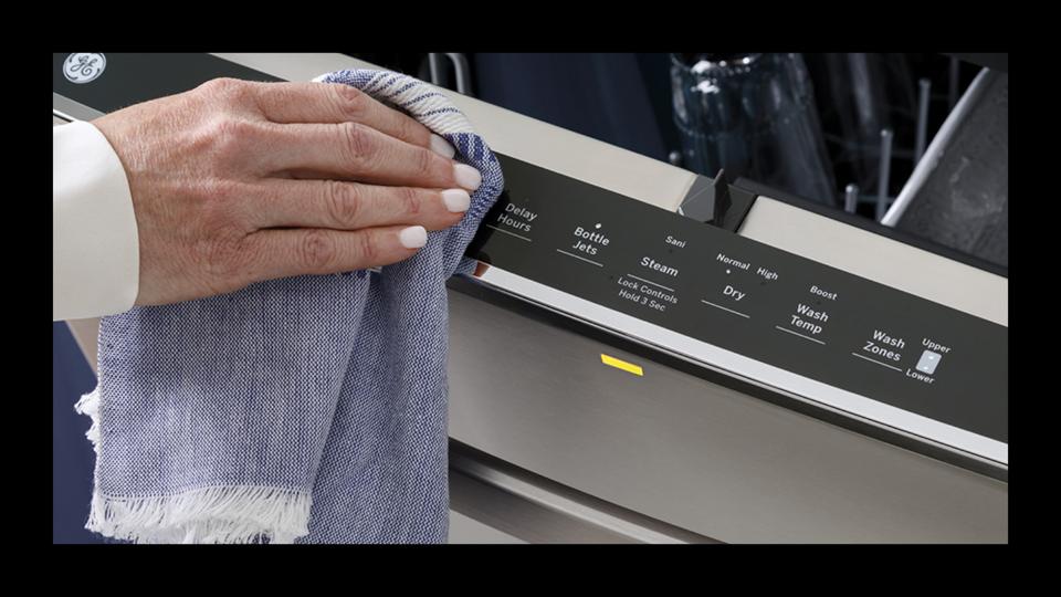 A woman using a dishcloth to wipe down her dishwasher. 