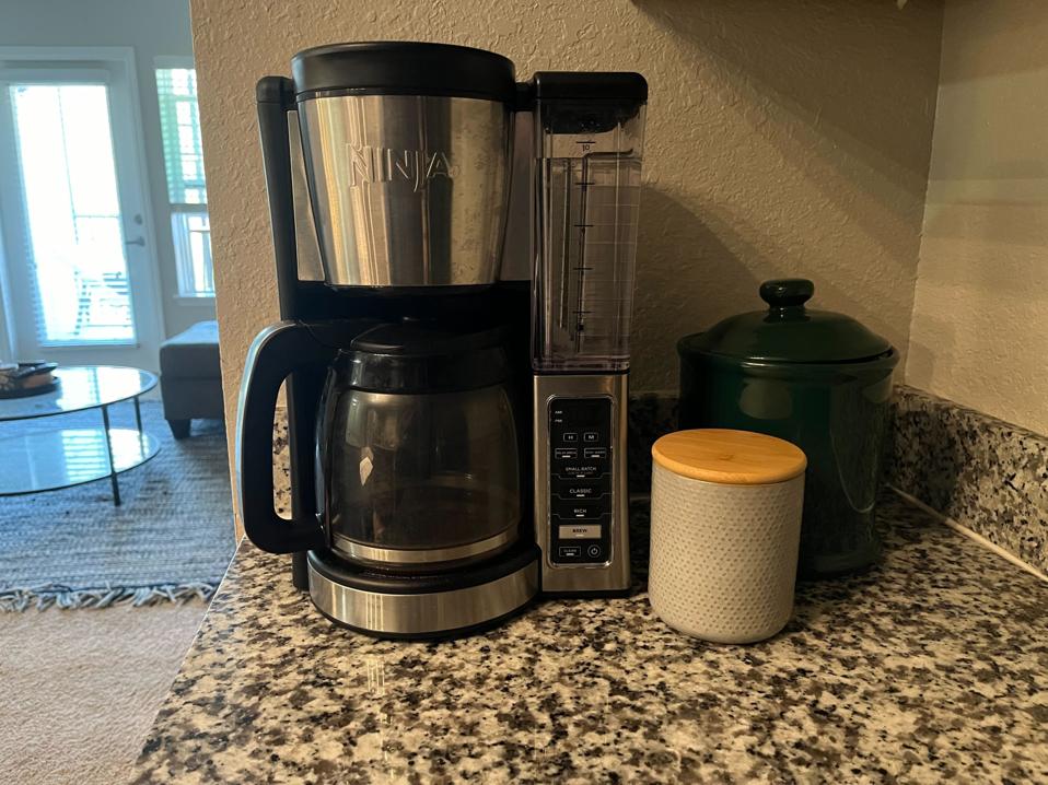 black ninja 12-cup drip coffee maker next to ceramic coffee containers on marble counter living room in background