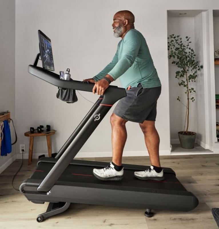 Man walking on an inclined Peloton Tread in a living room space. 