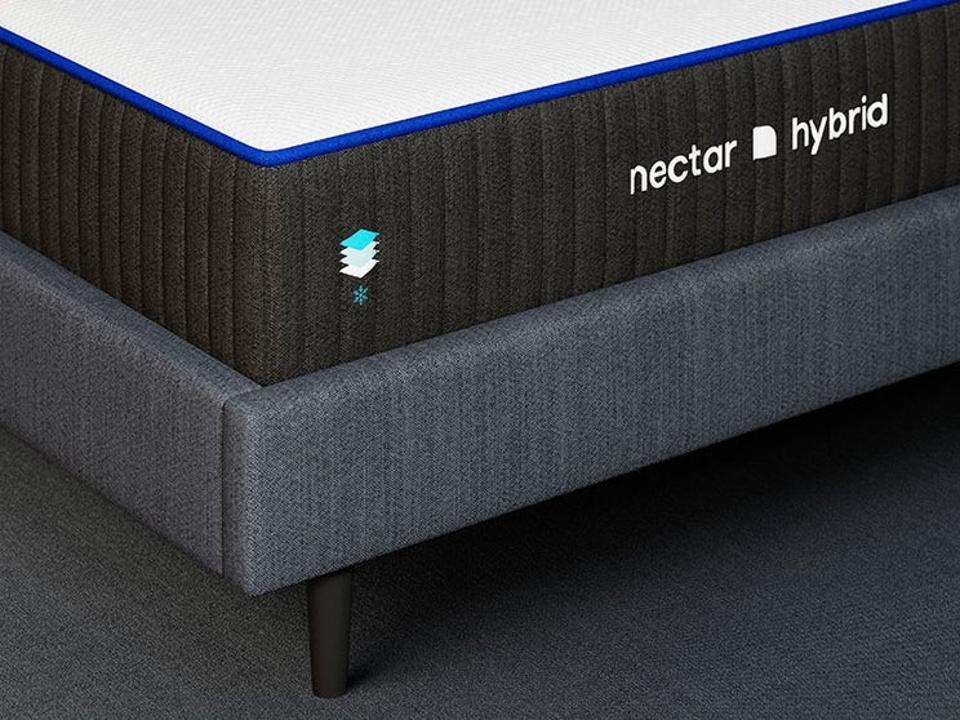 The corner of Nectar's hybrid mattress atop a grey bed frame on a grey carpeted floor.