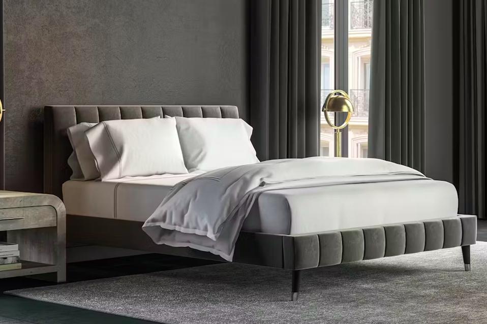 Saatva Valencia grey velvet upholstered bed frame against a grey wall with white sheets