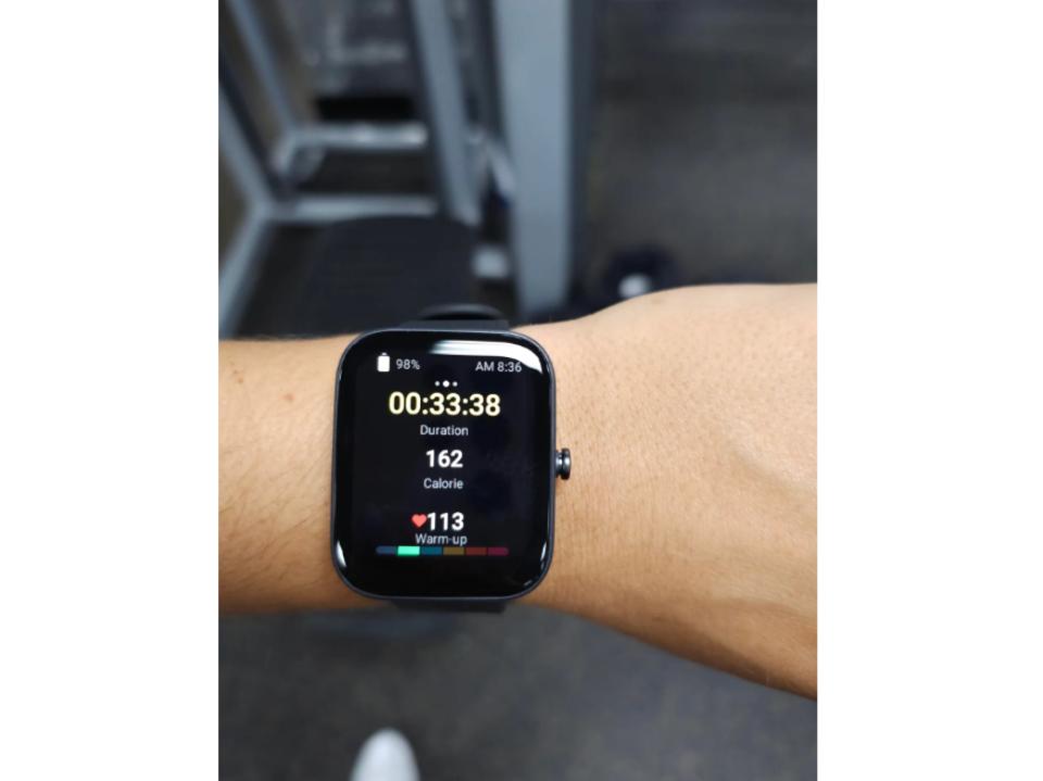 Amazfit Bip 3 Pro Smart Watch on left wrist of forbes vetted staffer with gym in background